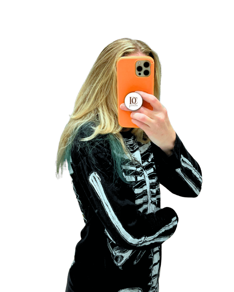 This is a decorative image of the author. Their face it hidden by an orange cellphone with a circle emblem containing the words, "DC Powers." The author has long blonde hair with green tips. Their wearing a black shirt white skeleton bones.